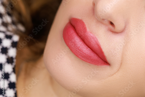 young model With a slight smile, on which permanent lip makeup is done with red pigment for tattooing