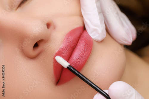 young model With a slight smile, on which permanent lip makeup is done with red pigment for tattooing