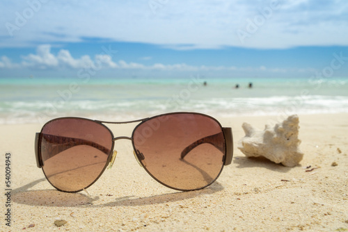 Sunglasses lie on the beach next to a blurred sea shell. Dark glasses on the background of a blurred sea and a cloudy sky. Vacation concept.