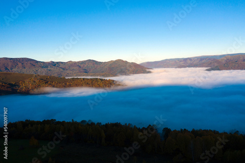 Flying above the clouds in dawn. Misty morning in the valley, aerial  view