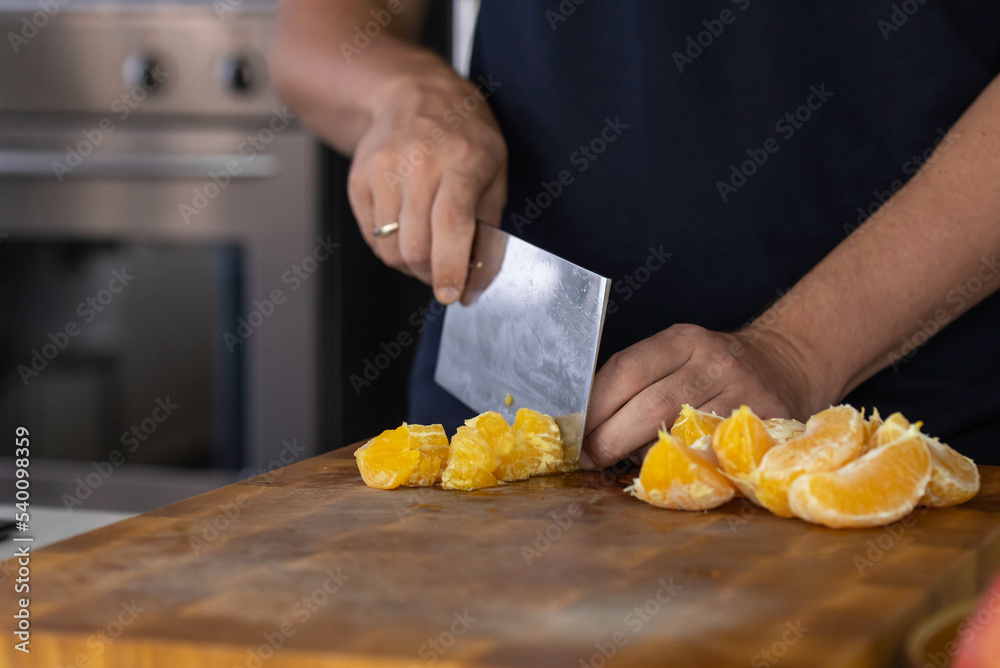Chef cook cutting fresh orange for fruit salad on wooden cut board Chef cook cutting fresh orange for fruit salad on wooden cut board