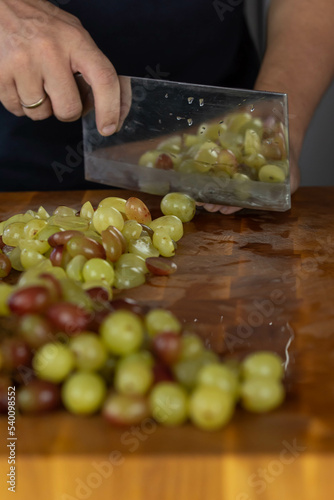 Chef cook cutting fresh grape for fruit salad on wooden cut board