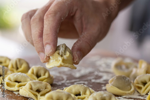Chef cook hands making handmade Tortellini ravioli on wooden cut board with flour. Italian cuisine.