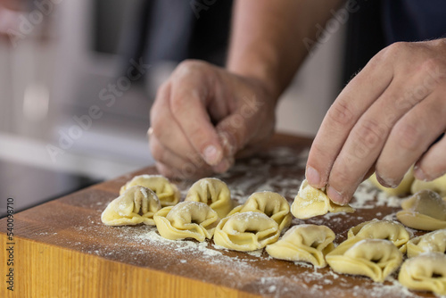 Chef cook hands making handmade Tortellini ravioli on wooden cut board with flour. Italian cuisine.