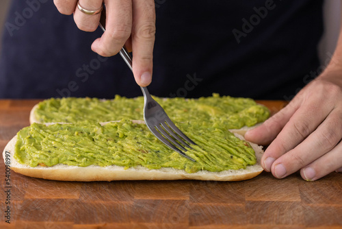 Chef cook hands making fresh diet avocado toast on bread with fork. Vegetarian and vegan cuisine. Healthy vitamin breakfast. photo