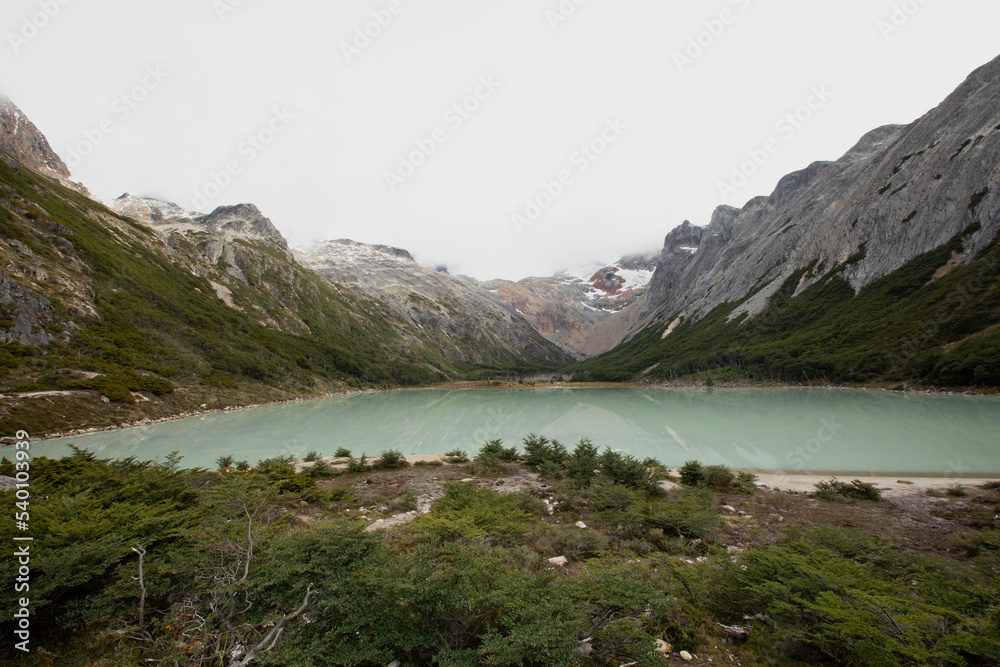 Panorama view of glacier water Emerald Lake i9n the mountaintop, in Ushuaia, Tierra del Fuego Patagonia Argentina. Turquoise color water lake surrounded by the Andes mountains and forest. Panorama view of glacier water Emerald Lake i9n the mountaintop, in Ushuaia, Tierra del Fuego Patagonia Argentina. Turquoise color water lake surrounded by the Andes mountains and forest.