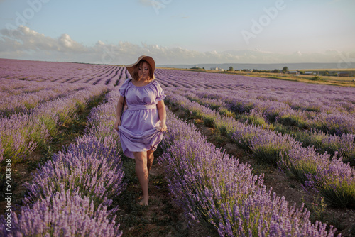 Fototapeta Naklejka Na Ścianę i Meble -  Beautiful plus size woman dressed purple dress and straw hat walking in the lavender flowers field, enjoy the aromatherapy in the meadow