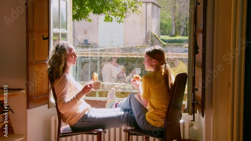 Woman showing something at the window to her teen daughter while drinking tea