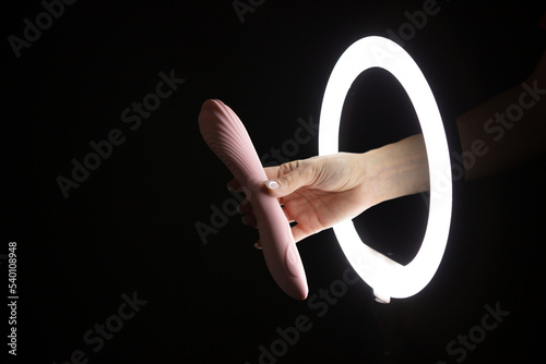 Female hand holding vibrator  through led ring lamp on black background. Sex concept photo