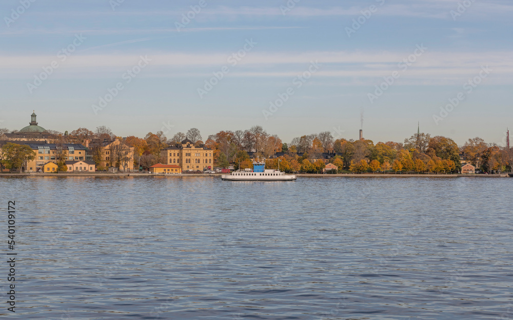 Harbor commuter ferry passing the island Skeppsholmen a color full autumn day in Stockholm