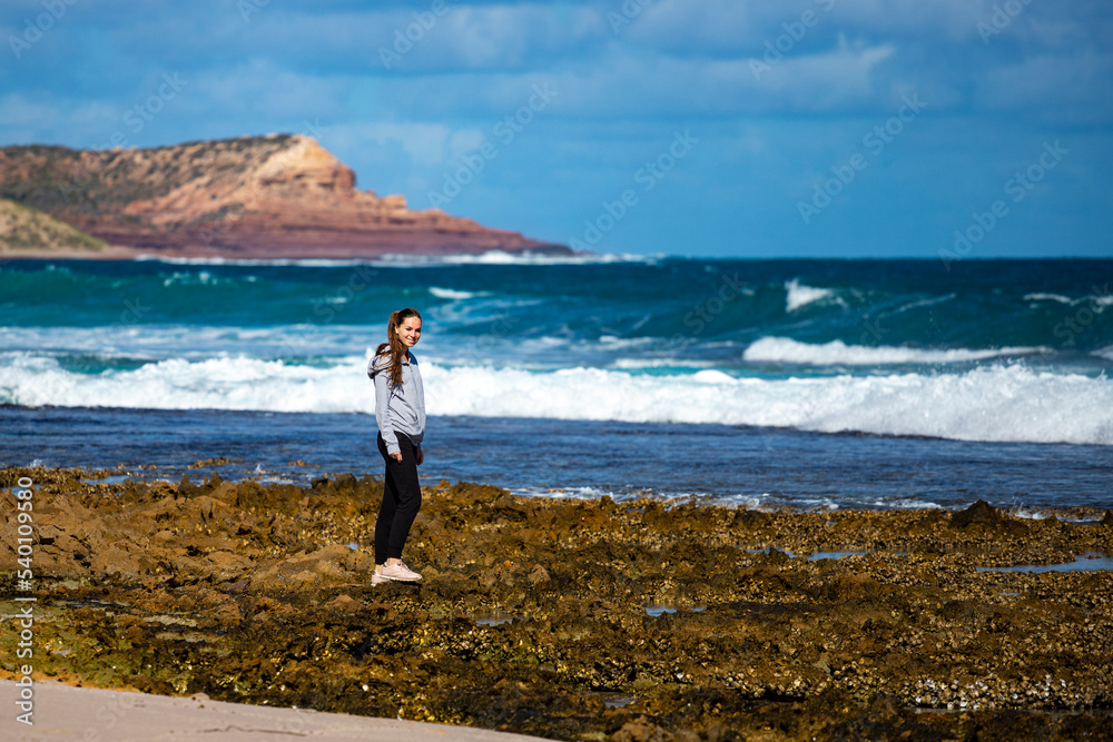 long-haired girl walks on the beach with massive cliffs in the background in kalbarri national park, western australia; walking on a paradise australian beach long-haired girl walks on the beach with massive cliffs in the background in kalbarri national park, western australia; walking on a paradise australian beach