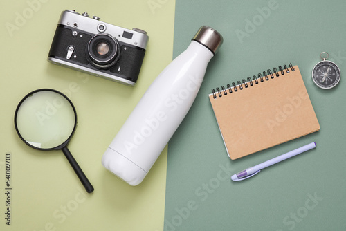 Hhiking equipment. Thermos bottle, camera, magnifier, notebook and compass on green background. Top view. Flat lay photo