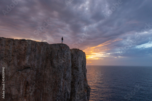 views from drone, with person standing on cliff enjoying the sunset on the Menorcan coast.