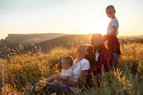 Happy family spending time together in the nature, mother father daughter and son have fun, playing with kids in vacation against the background the grass, mountain and sunset