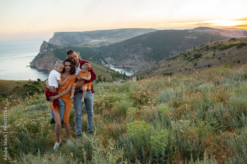 Happy family spending time together in the nature, mother father daughter and son have fun, plying with kids in vacation against the background the grass, mountain and sunset