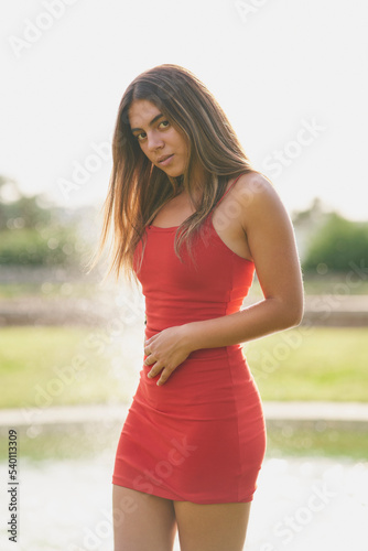 Girl with tight red dress and long straight hair posing in a park