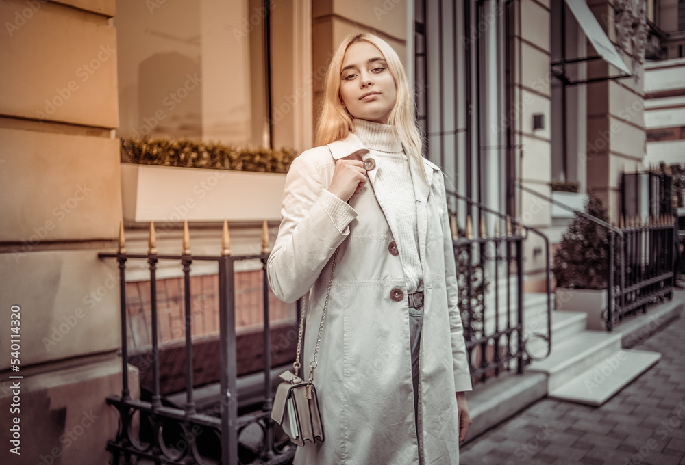 Portrait of a young fashion blonde woman in an autumn trench coat against the background of urban architecture Portrait of a young fashion blonde woman in an autumn trench coat against the background of urban architecture