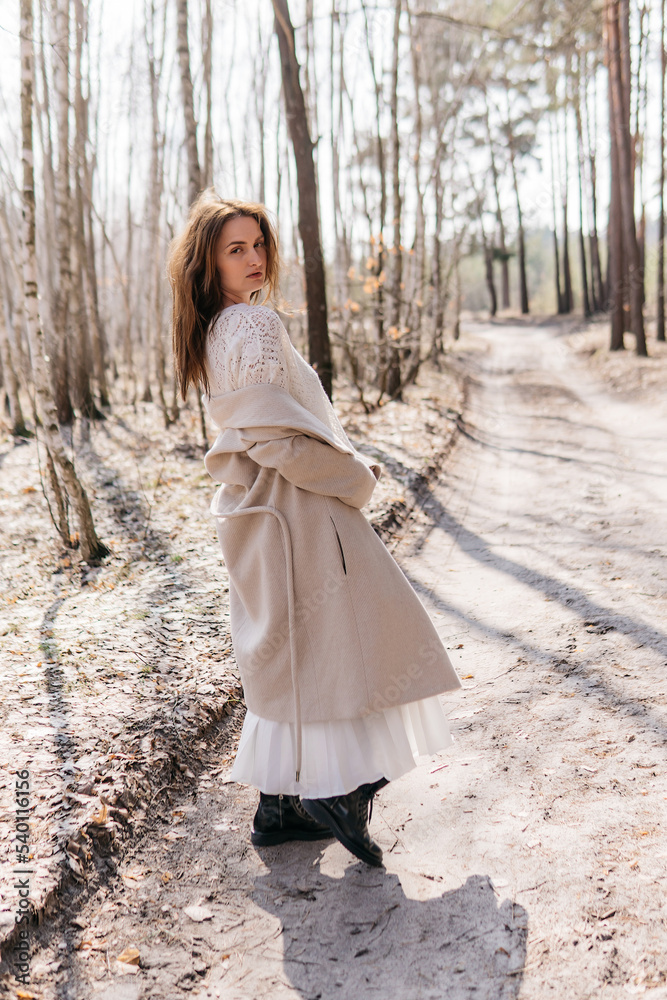 Beautiful girl in a white dress and a beige coat in a spring birch grove. High quality photo