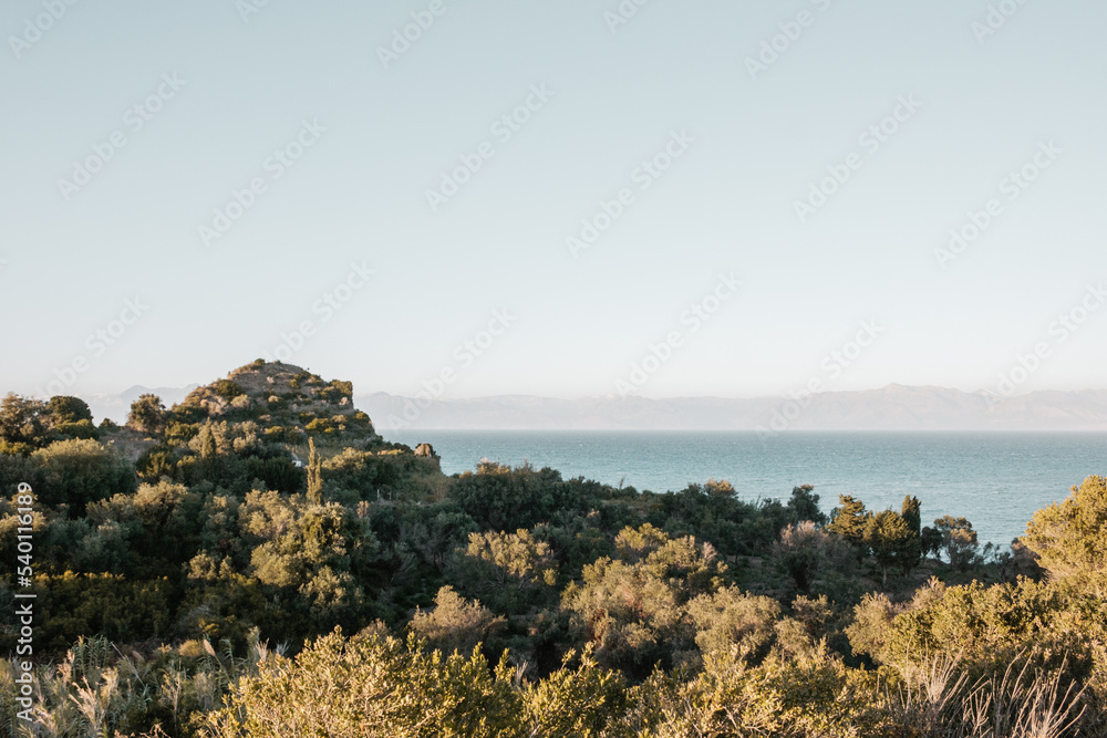 Beautiful view of the sea in Greece with mountains on the horizon and green bushes and mountains in the foreground.