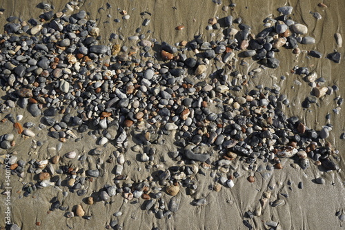 Sunny autumn day on the Aegean Sea. Texture of wet pebbles on beach sand. Surf