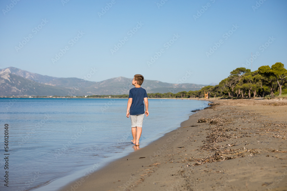 Boy playing on the beach on summer holidays. Children in nature with beautiful sea, sand and blue running in the sea water.