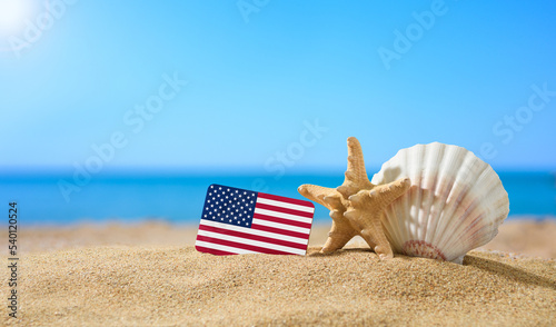 Fototapeta Naklejka Na Ścianę i Meble -  Tropical beach with seashells and flag of the United States. The concept of a paradise vacation on the beaches of USA.