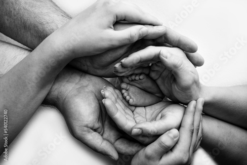 Baby feet in the hands of mother, father, older brother or sister, family. Feet of a tiny newborn close up. Little children's feet surrounded by the palms of the family. Parents and their child. 
