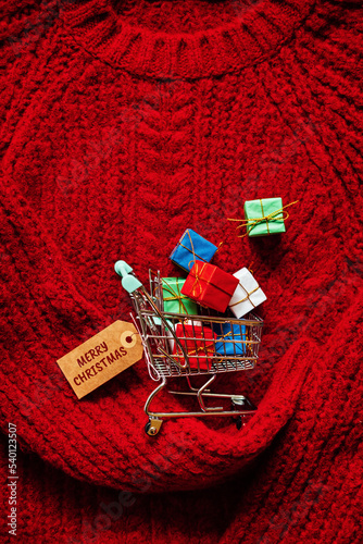 Christmas xmas early sale shopping concept. Shopping cart with many gift boxes on red knitting background photo