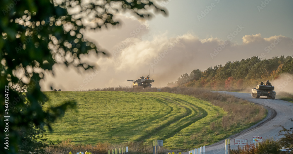 a section of British army Challenger 2 ii FV4034 tanks descend a country track to a road crossing, late afternoon autumn sky, Wiltshire UK