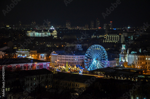 Aerial evening view to Kontraktova Square with Christmas market, New Year tree and ferris wheel during celebration. Kyiv, Ukraine