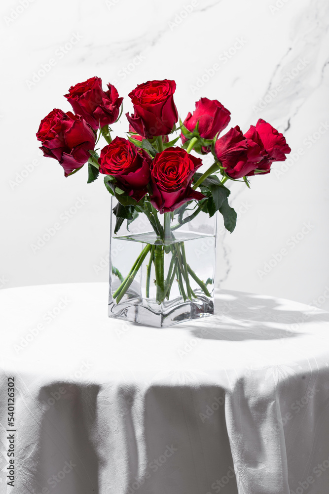 Fototapeta premium Red roses in a vase on a round table on a white background