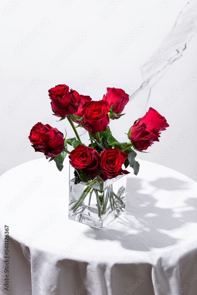 Fototapeta premium Red roses in a vase on a round table on a white background