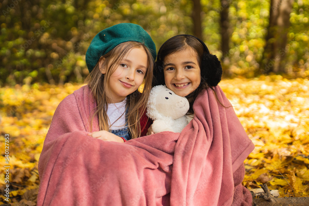 Two sisters in the forest covered with a blanket are sitting next to each other. Two little sisters. Generation z. sisterhood Happy childhood. Two sisters in the forest covered with a blanket are sitting next to each other. Two little sisters. Generation z. sisterhood Happy childhood.