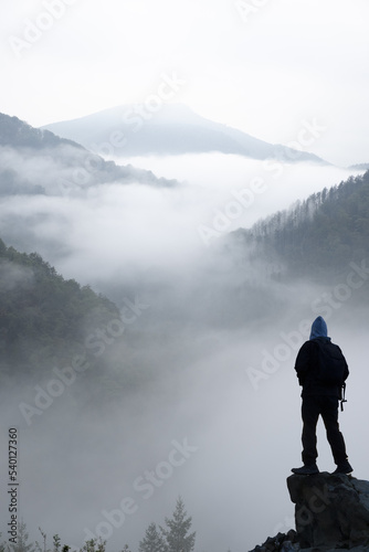 Hiker looking at the cloudy and misty landscape between the mountains.