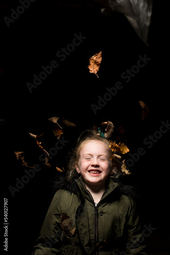 Young girl throwing dying leaves in the air at autumn time in a studio setting.