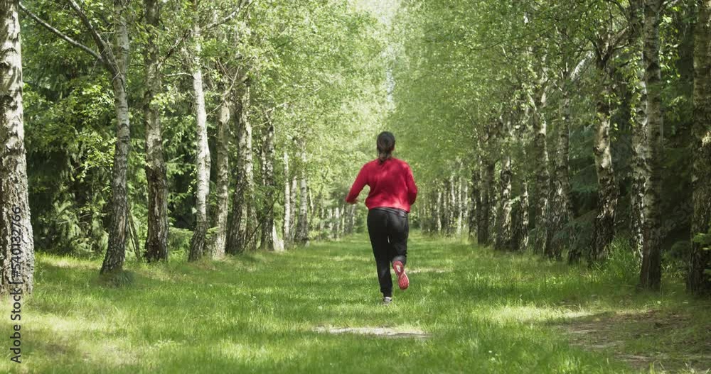 Happy woman in a red sweater runs on a birch forest path.
Happy woman in a red sweater runs on a birch forest path.