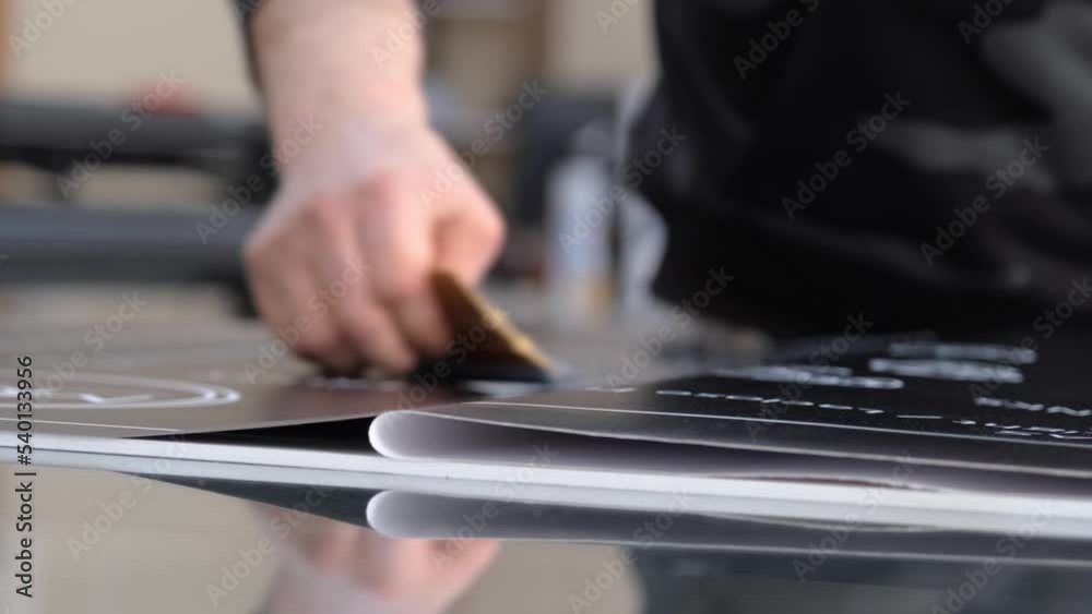 Advertising image printing paste. The man applying the vinyl printing foil to the material surface using a felt squeegee. 