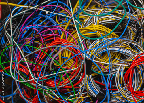 Colored telecommunication cables and wires tangled in a tangle in a box. The multicolored wires and cables in the box are mixed up and tangled into knots.