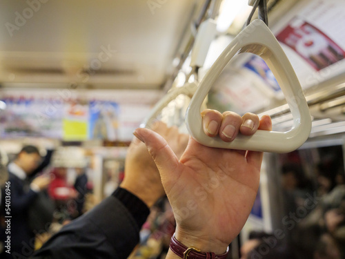 Hands holding on to handles to support themselves while standing on a busy subway train