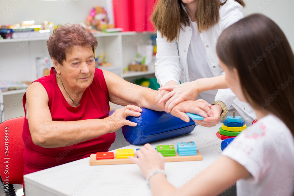 Old woman suffering from stroke exercising on physiotherapy with help of physiotherapist in the hospital Old woman suffering from stroke exercising on physiotherapy with help of physiotherapist in the hospital