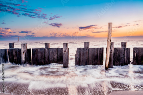 Oceanscape with wooden breakwater along shoreline beach coast at sunset