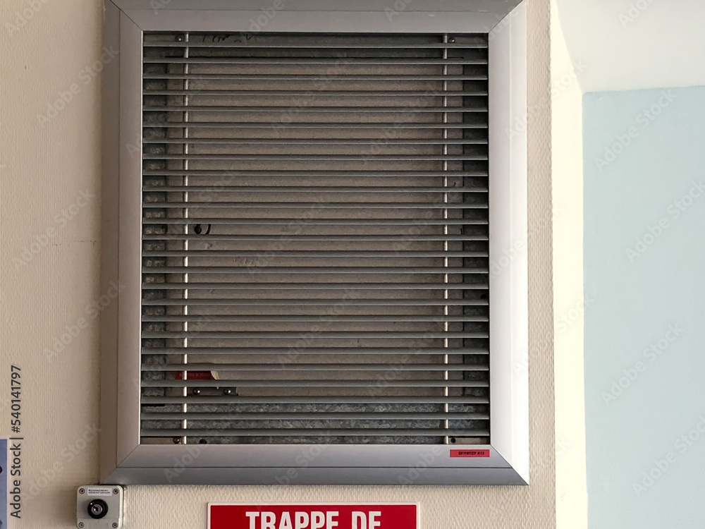 illustration d'une trappe de désenfumage de couleur grise sur un mur avec sa pancarte en dessous de couleur rouge et blanche