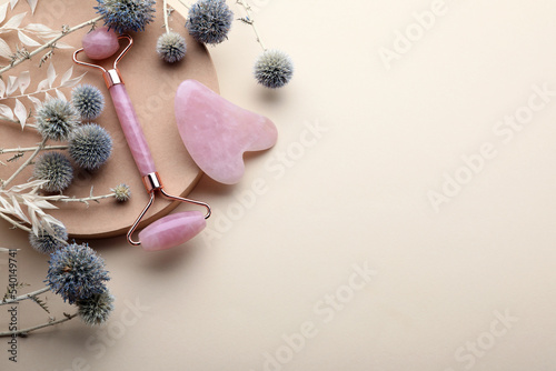 Flat lay composition with rose quartz gua sha tool and facial roller on beige background. Space for text