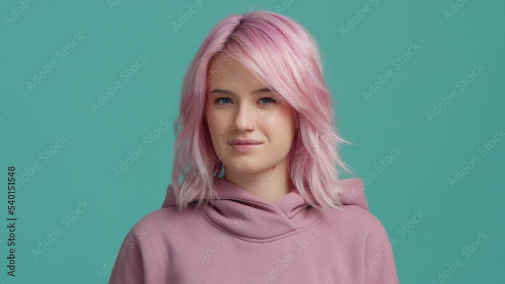 Slow motion studio shot pink haired young woman of 20s in pink hoodie looking straight into camera and showing zipping, closing mouth gesture visualizing silence, stop do not want talk in slow motion Slow motion studio shot pink haired young woman of 20s in pink hoodie looking straight into camera and showing zipping, closing mouth gesture visualizing silence, stop do not want talk in slow motion