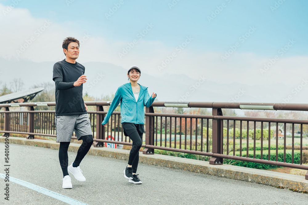 健康のため公園でウォーキング・散歩・有酸素運動するスポーツウェアを着たアジア人の男女
