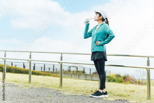 公園で有酸素運動中にミネラルウォーター・スポーツドリンクを飲むアジア人女性 