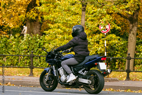 A man rides a dark blue motorcycle on the road near the autumn park. Last days for motorcyclists before winter  closing of the season.