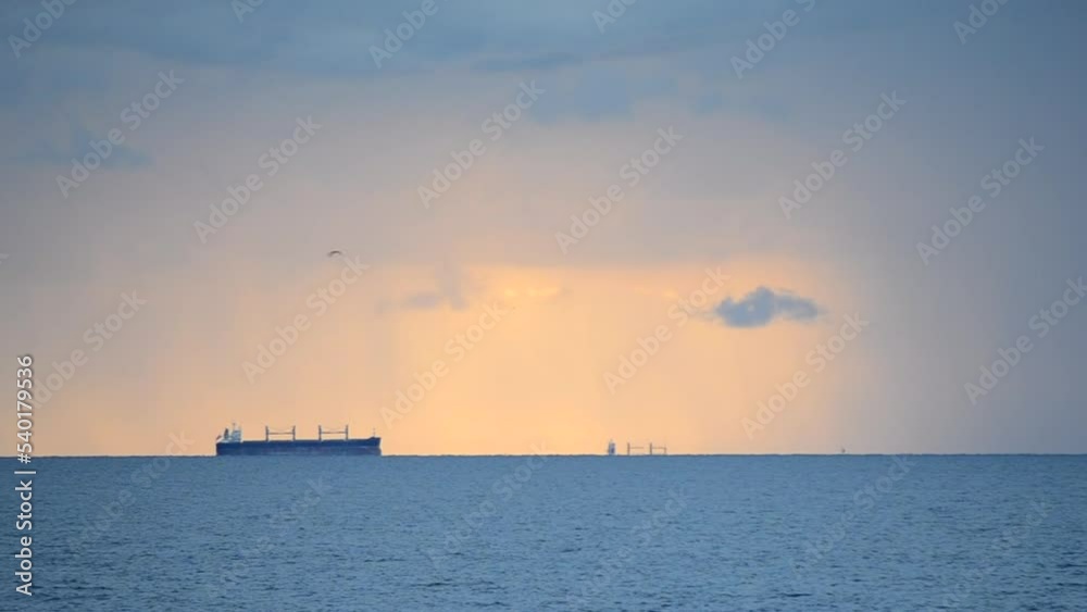 A grain-carrier tanker is far away on the horizon line in the sea against the background of a dawn sunset with falling rain and large dark thunderclouds. Seascape, sea landscape. Natural background A grain-carrier tanker is far away on the horizon line in the sea against the background of a dawn sunset with falling rain and large dark thunderclouds. Seascape, sea landscape. Natural background