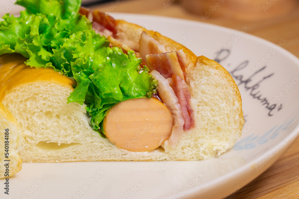 Hotdog with bacon and sausage on white plate Hotdog with bacon and sausage on white plate