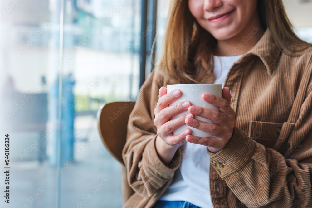 Closeup image of a young woman holding and drinking hot coffee in cafe Closeup image of a young woman holding and drinking hot coffee in cafe